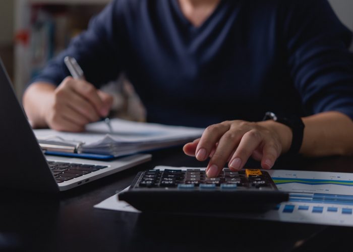 Businessman using a calculator and writing financial data. Budget planning, accounting, tax calculation, expense tracking, and financial management for corporate and personal finance. Man calculating expenses and managing financial documents. Tax return preparation, budget tracking, cost management, financial investment, and economic strategy analysis.